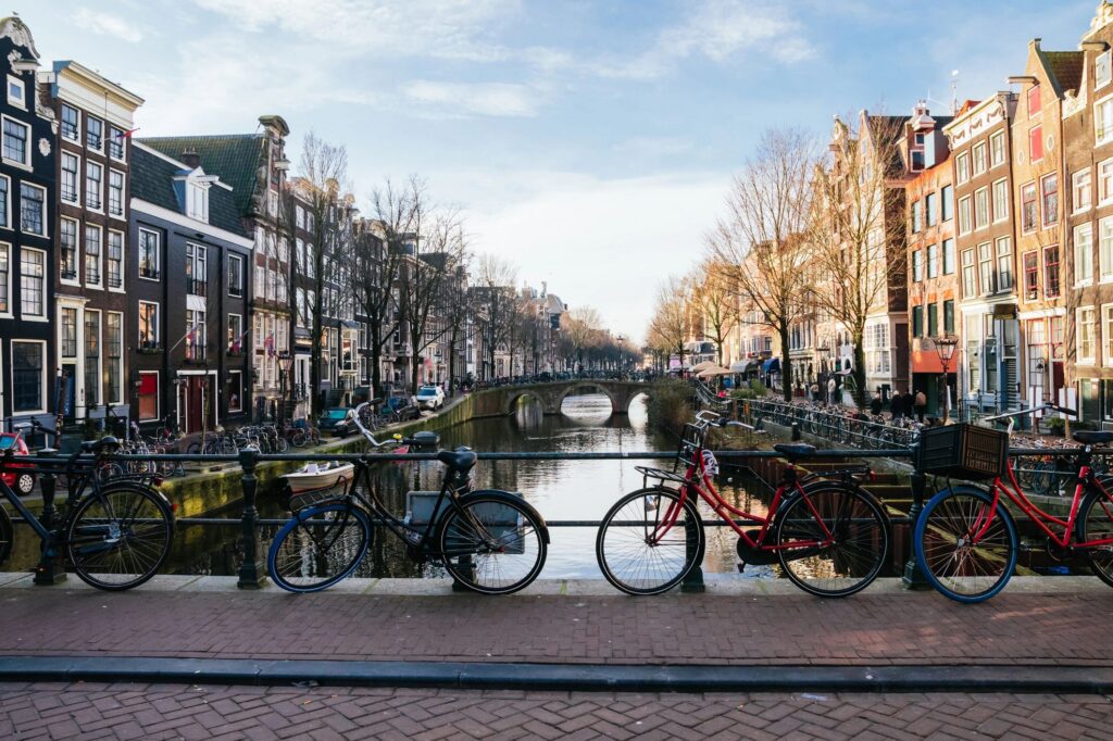 Bicycles lining a bridge over an amsterdam canal, showcasing the city's iconic architecture and reflecting its sustainable urban lifestyle with water, narrow houses, and tree-lined streets